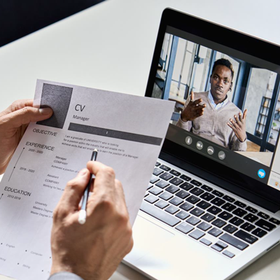 Laptop screen showing a candidate being interviewed. A copy of a CV is in the foreground.