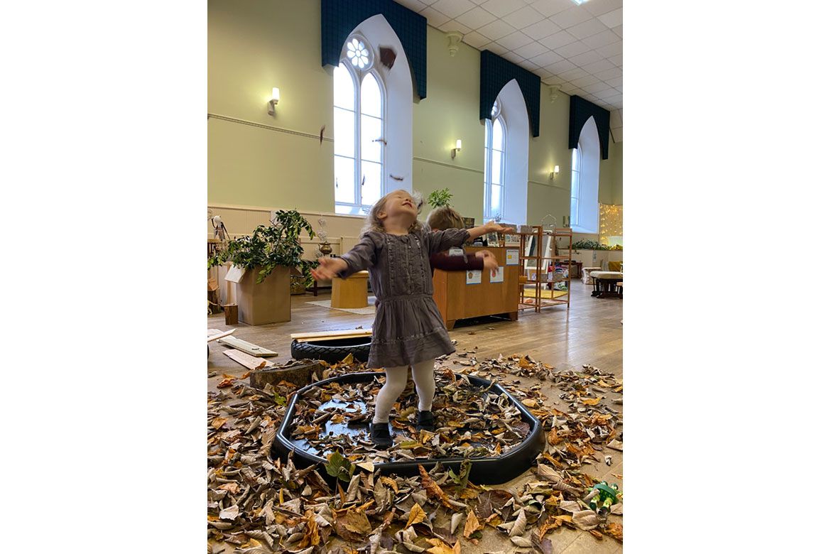 Young girl plays with leaves at Strathisla Children's Centre