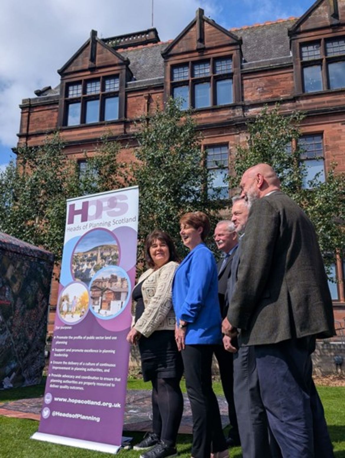 Four people in business wear standing beside a Heads of Planning Scotland banner
